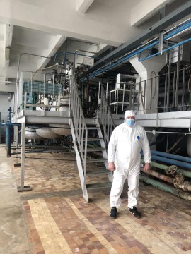 На малюнку зображено співробітника в білому захисному костюмі та масці у виробничому приміщенні