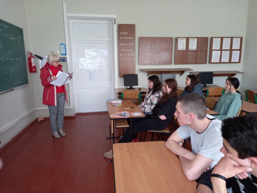 На малюнку шкільна класна кімната, жінка розповідає підліткам