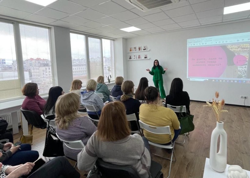 На малюнку зображена ведуча біля дошки и люди в залі, що дивляться на неї