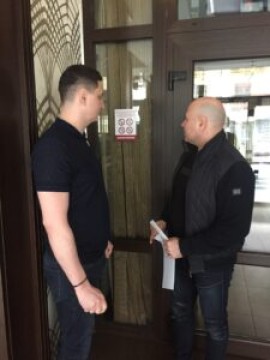 На малюнку два чоловіка в приміщенні кафе дивляться на пам'ятку про заборону куріння