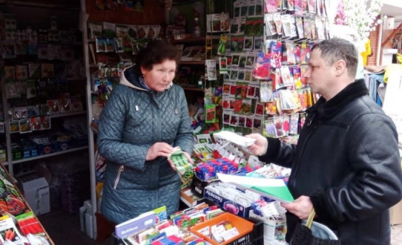 На малюнку зображено крамницю з насінневим матеріалом в пакетиках, продавця і фахівця Держпродспоживслужби