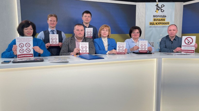 На малюнку зображені ведучі конференції з табличками про заборону куріння в руках