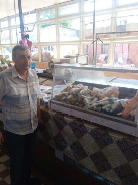 на фото чоловік біля прилавку з рибою
