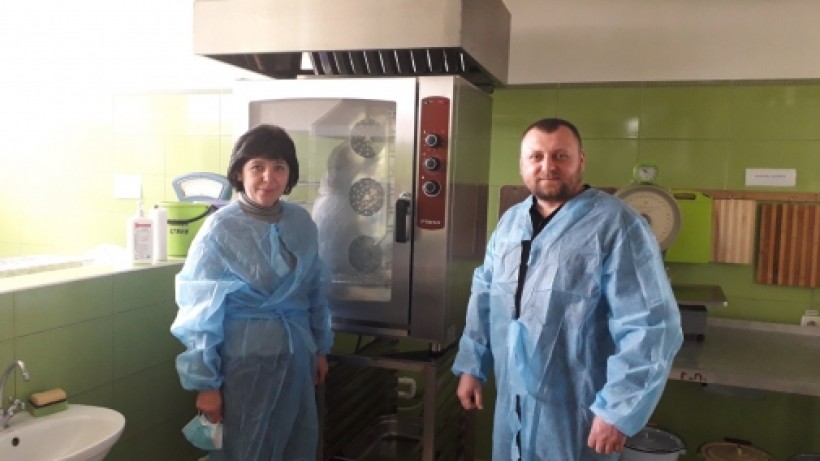 на малюнку - дві людини в захисних халатах в приміщенні шкільної кухні