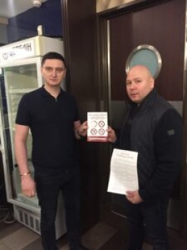 На малюнку два чоловіка в приміщенні кафе з пам'яткою про заборону куріння