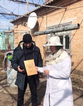 На малюнку зображено фахівця в спецодязі пасічника дає документ чоловіку