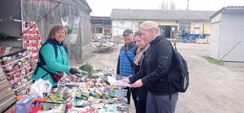 на малюнку три жінки і чоловік біля ятки з насінням в пакетиках