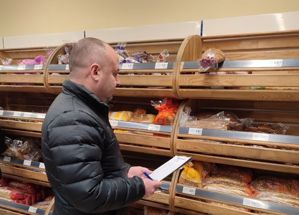 на малюнку - чоловік з папкою в магазині біля полиць з хлібом